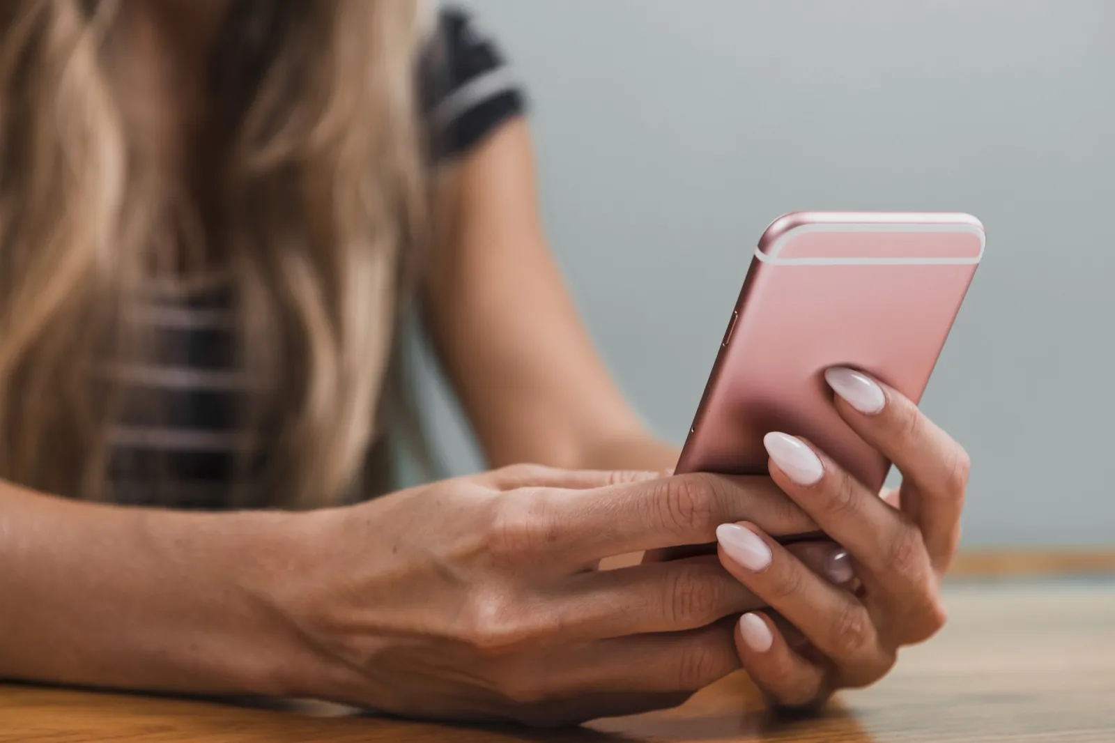 Two hands typing a message on a pink phone at a table.