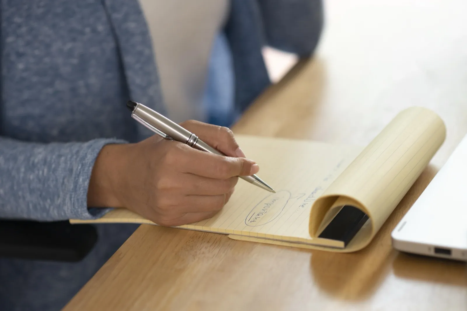 A hand writes on a yellow pad, one word circled.