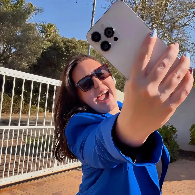 Georgia May in a blue blazer, holding a phone up to take a photograph.